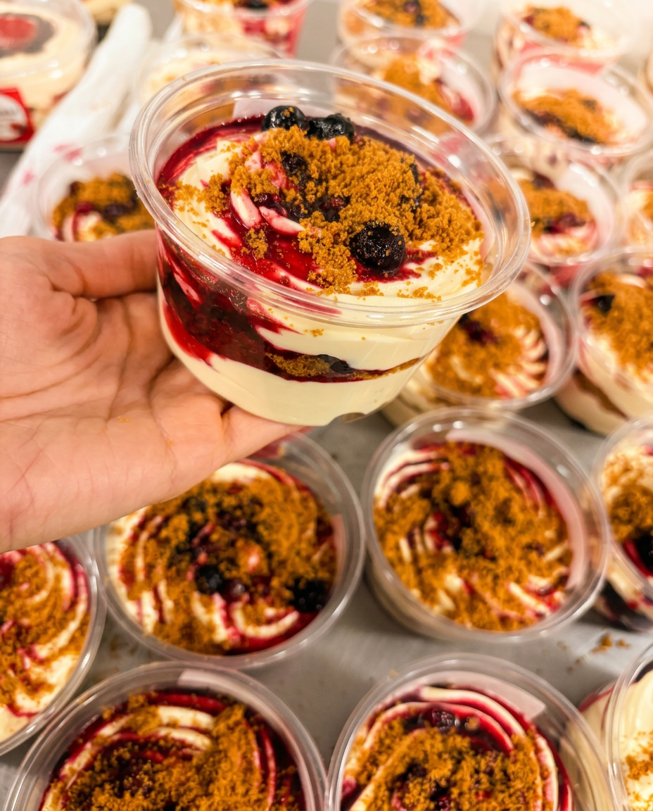Un pot de tiramisu fruits rouges & spéculoos Dolcini tenu en main au-dessus de la production